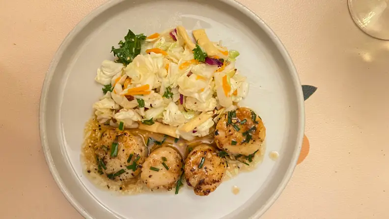 In the center of the image, there's a plate with four pieces of scallops accompanied by salad.