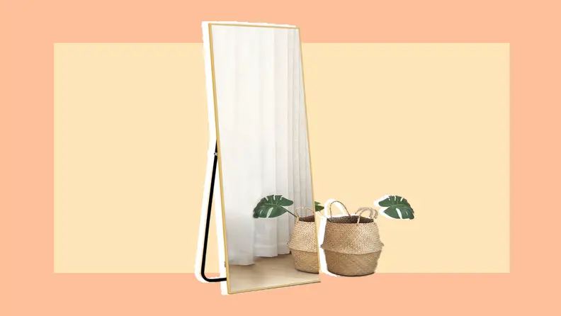 Freestanding rectangle-shaped mirror wall next to straw bin and palm frond.