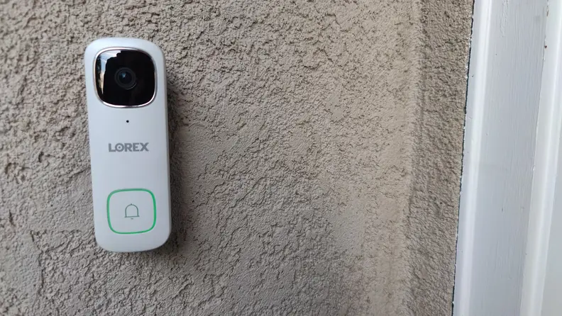 White Lorex 2K Wired Video Doorbell mounted on wall on home outdoors.