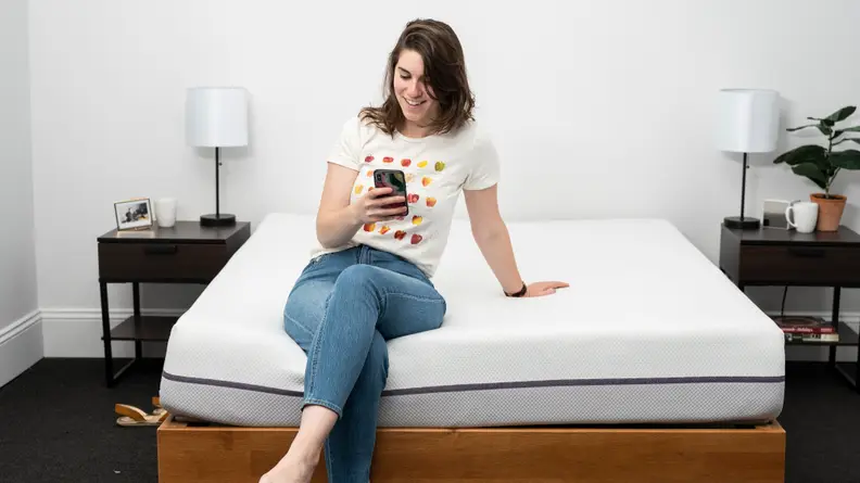 a person sits on the end of the Purple mattress on their phone