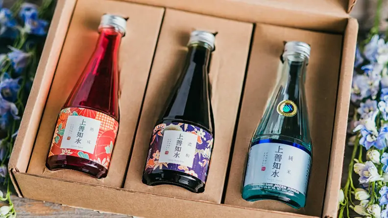 A cardboard box containing three bottles of sake, artfully framed by flowers.