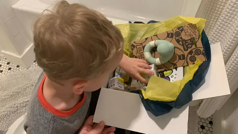 A small child peruses a box of bath toys.