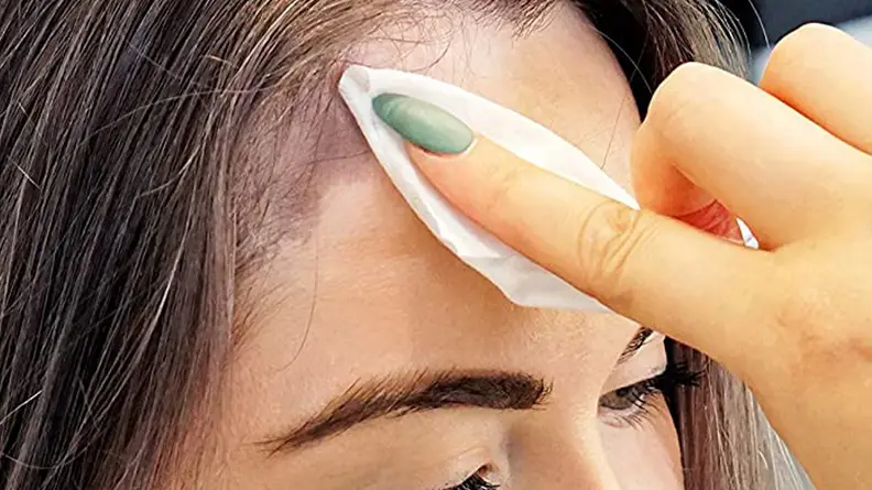 A closeup on a person's forehead with a hand gliding a wipe along the skin to remove hair dye.