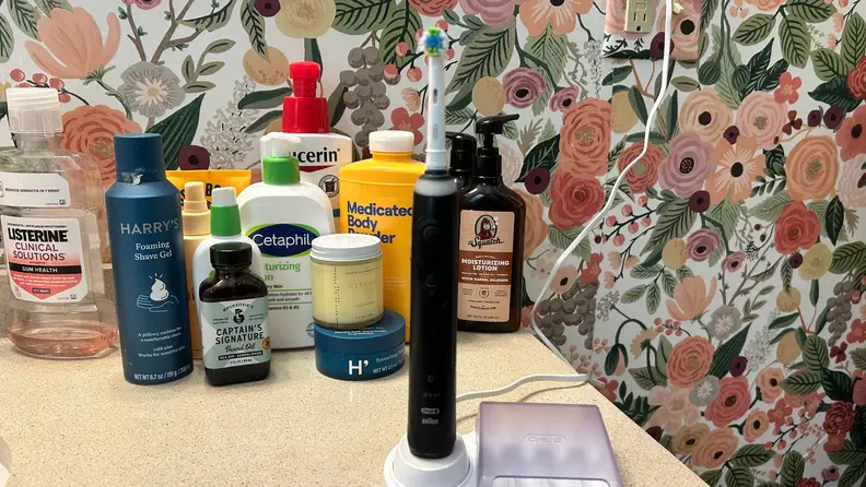 A black toothbrush sits on a bathroom counter with cosmetics in the background
