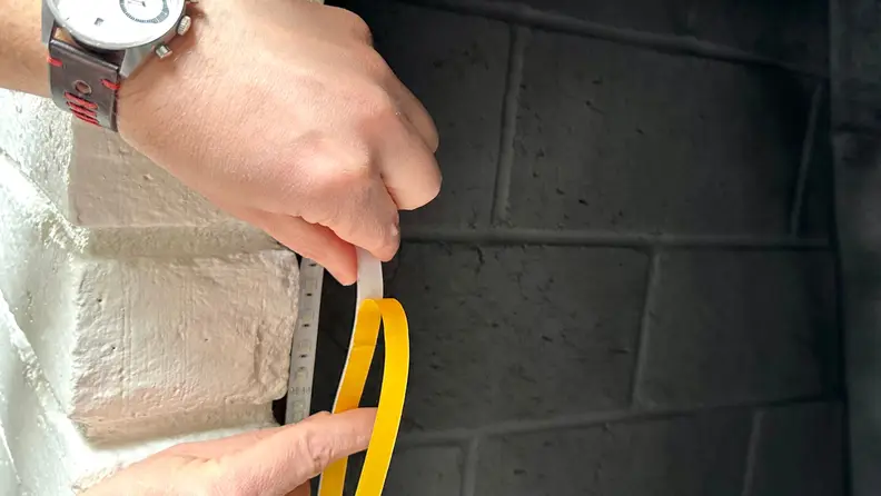 A pair of hands sticking the strip lights around a fireplace.