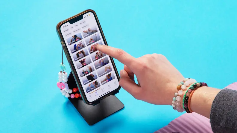 Person using finger to navigate the FitOn fitness app on smart phone.