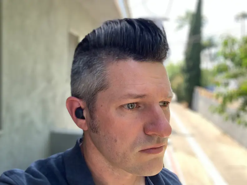 A man in a blue shirt listens to the black Sony LinkBuds S while standing on a balcony.