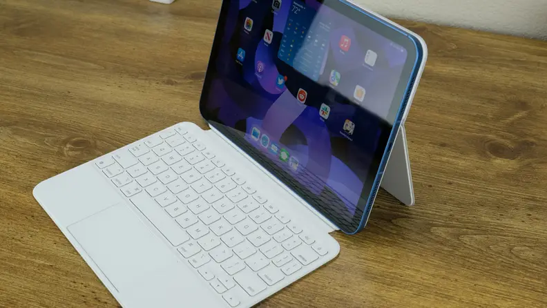 The blue Apple iPad 10 sits on a wooden desk with its white keyboard.