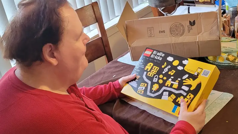 A man holding the LEGO Braille Bricks box.