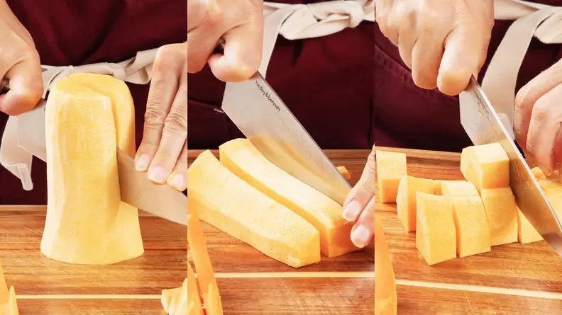 Person using knife to cut the neck section of butternut squash in half and then into cubes on top of wooden cutting board.