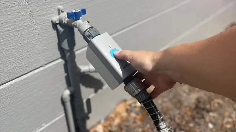 Someone pressing the button on the front of the  Rachio smart hose timer