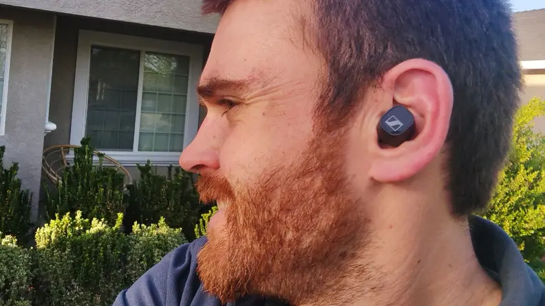 Sennheiser CX Plus earbuds sitting in an ear in front of greenery.