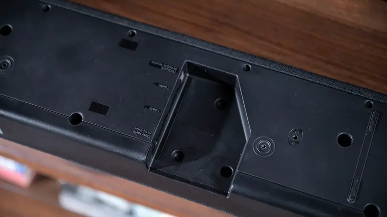 The black Q950a sits on a woodgrain cabinet with a cut-out for its inputs showing.