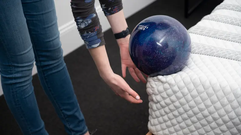 Hands catch a bowling ball that's about to roll off the edge of the mattress.