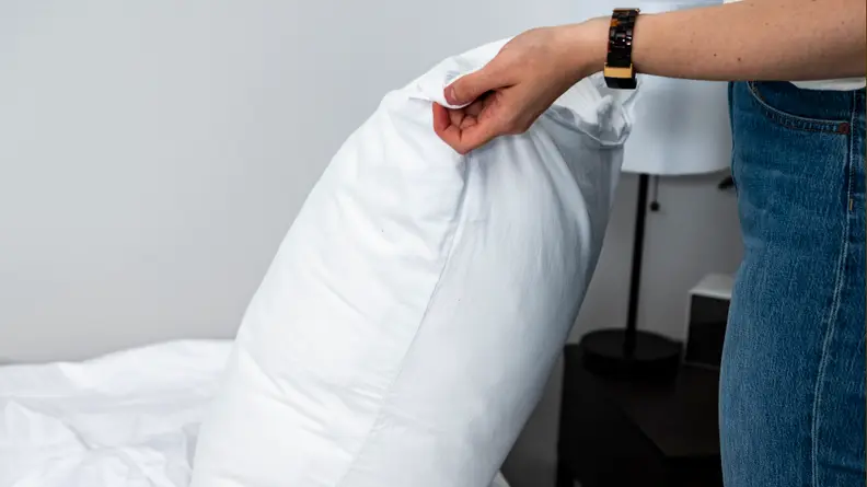 a person's hands hold the brooklinen pillow protector over a pillow