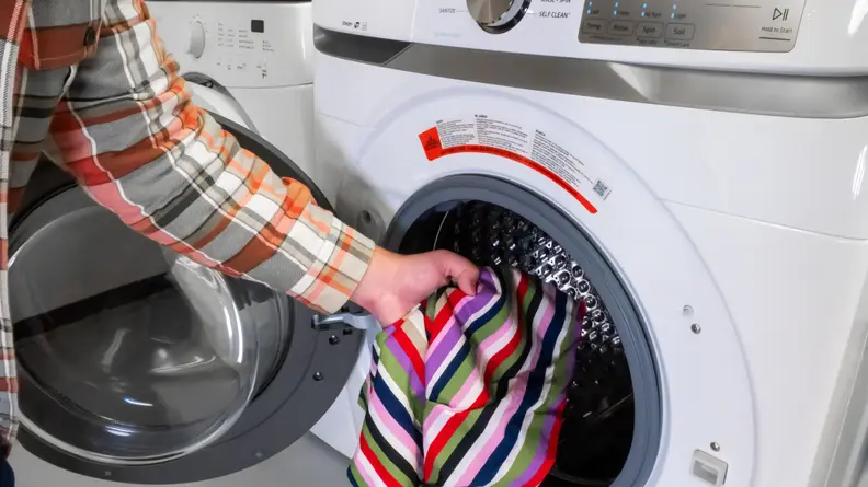 Someone throwing a brightly-colored towel into the Samsung WF45R6100AW washer.