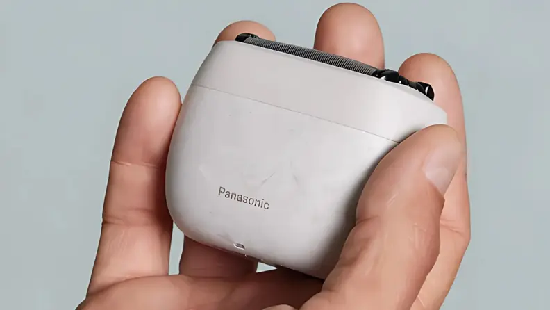 A hand holding a compact Panasonic electric shaver for men against a plain background.