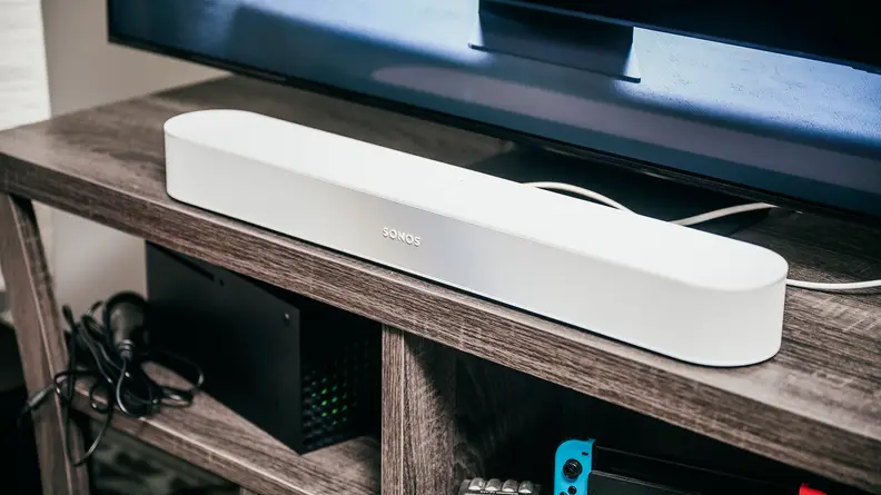 The Sonos Beam Gen 2 sitting on a TV stand in front of a TV playing content