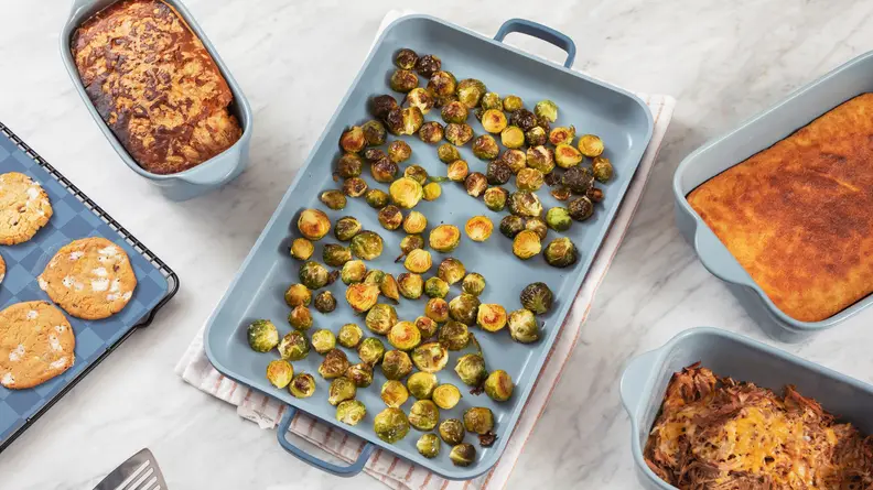 A griddle pan with Brussels Sprouts sits at the center of a radial arrangement of Our Place Bakeware full of baked goods.