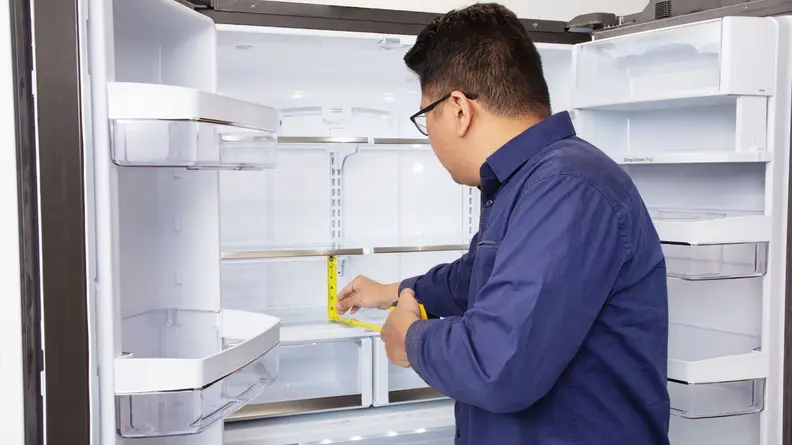 Lab technician measures shelf height inside of refrigerator with measuring tape.