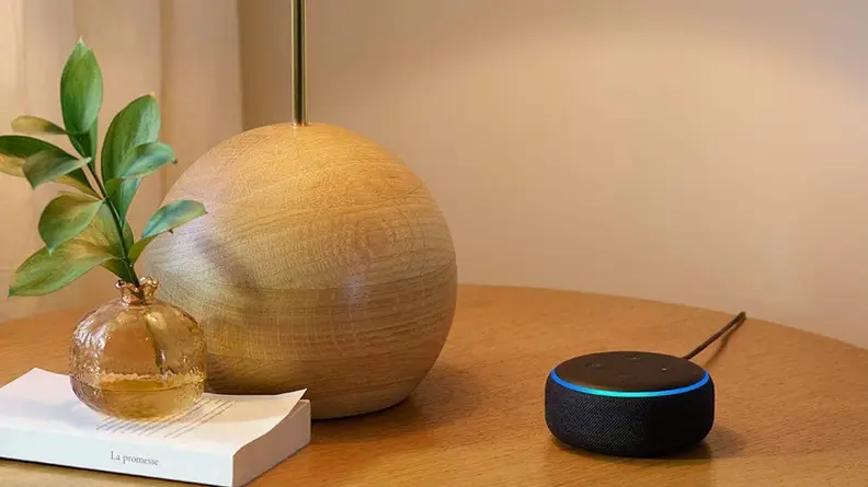 An Echo Dot on a side table next to a book.