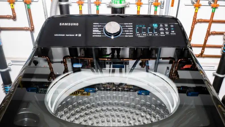 A shot of the top lid of the Samsung WA50R5400AV top-loading washing machine. In the background you can see the elaborate network of pipes we use to regulate water temperature and flow.