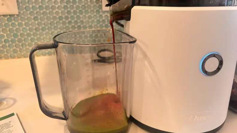 The Omega Effortless Batch Juicer dispensing a juice into a large glass measuring cup.