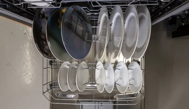 A top-down shot of the Hisense HUI6220XCUS dishwasher, with its door open and bottom rack pulled out. There you can see several place settings stowed away.