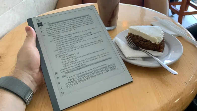 A reMarkable 2 tablet is held in someone's hand while they have a cup of coffee