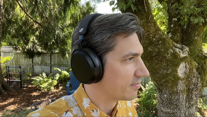 A person wearing the Sennheiser Momentum 4 outside in a backyard.