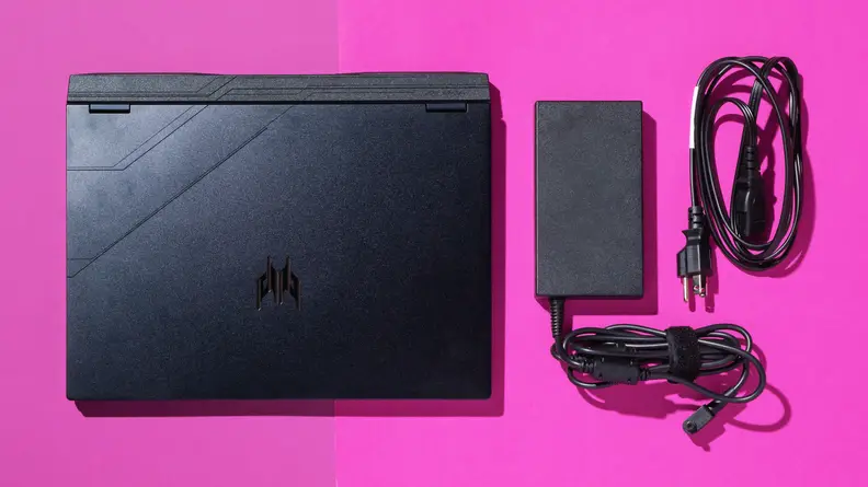 A black Acer Predator Helios Neo 14 gaming laptop with the power cable next to it, on a pink table