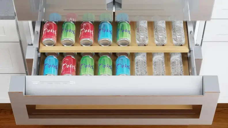 Two rows of canned soft drinks and bottles of water lined up inside of Flex Drawer on stainless steel refrigerator.
