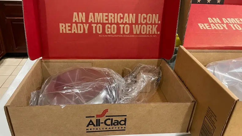 All Clad cookware inside of cardboard box.