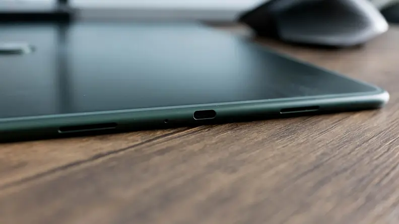 A tablet computer sits, face down on a table, it's charging port in view