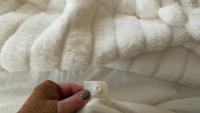A hand holds up a snap on a bedspread