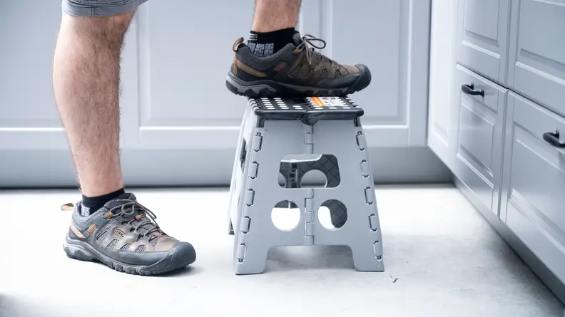 A person wearing sneakers steps on a low plastic stool