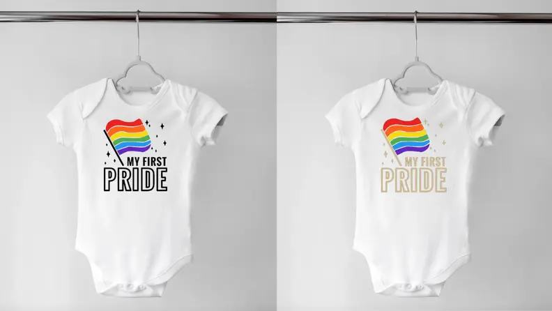 Two white onesies hanging on a hanger with a rainbow flag on it and the words "My First Pride" written on it