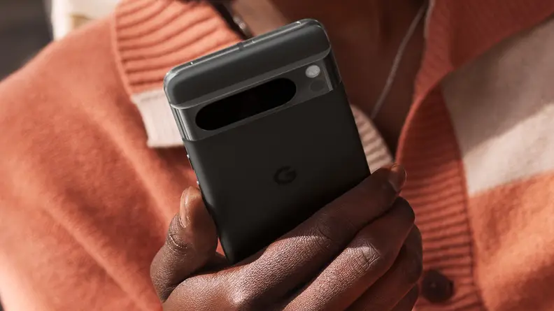 An individual holds a black Google Pixel 8 Pro smartphone. The camera array on the backside of the handset is visible.