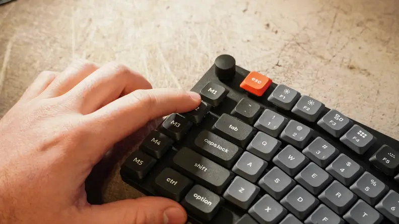 A hand touching the volume knob on a keychron k15 pro keyboard