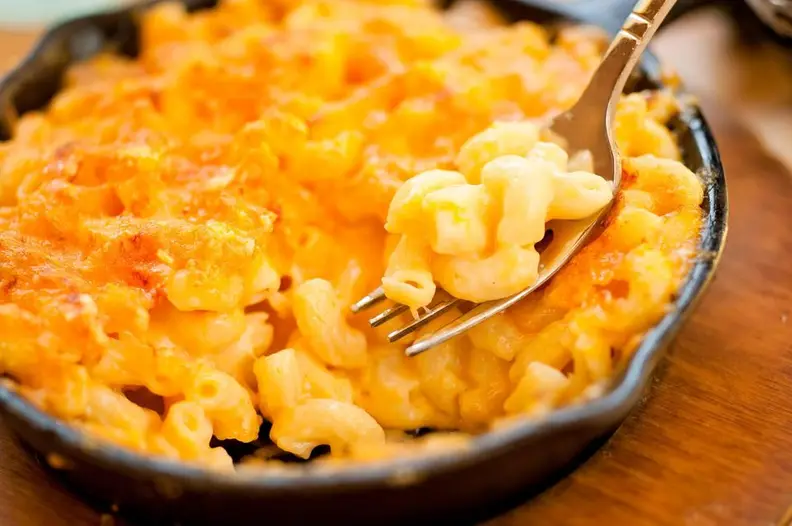 A cast iron pan full of macaroni and cheese is in the center of the image.