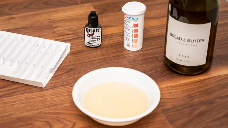 A piece of paper, a bottle of Drop It wine drops, testing strips and testing wine gathered together