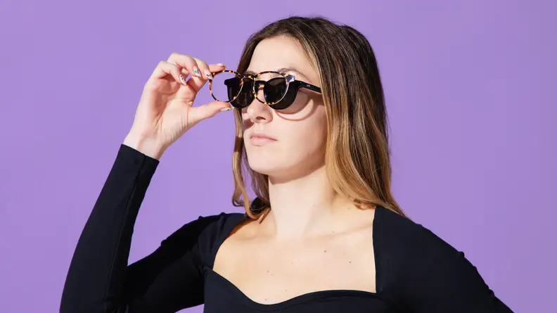 Woman wearing black shirt and pair of eyeglasses in front of purple background