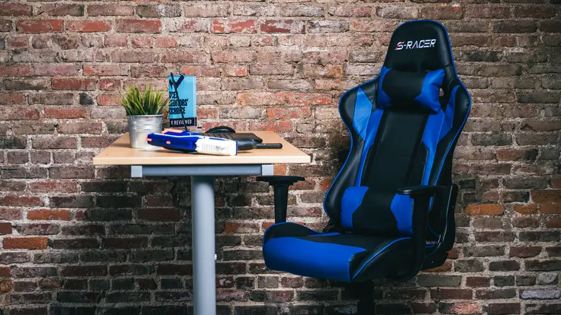 The Homall Gaming Chair, a blue and black gaming chair with racecar seat-like fins, against a brick wall