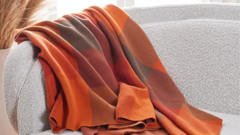 An image of an orange and deep red checked blanket draped over a sofa.