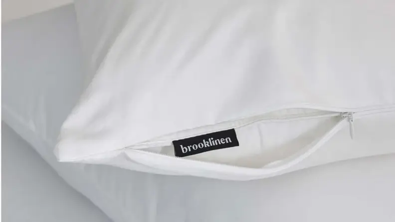 the zipper on a brooklinen pillow protector opened to reveal the tag on a pillow beneath