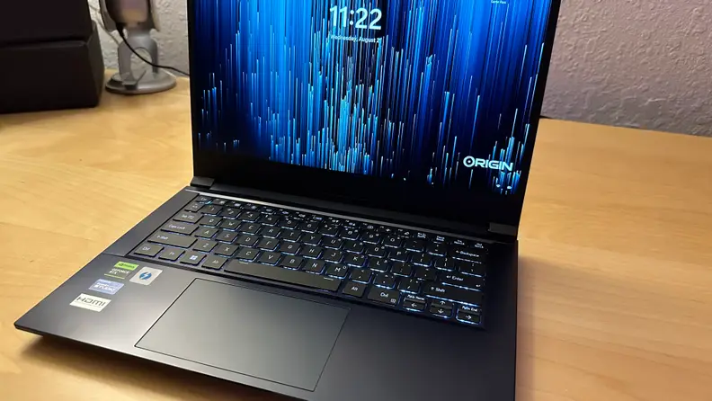 Origin EON14-S gaming laptop sitting on top of wooden surface with clock screen display turned on.