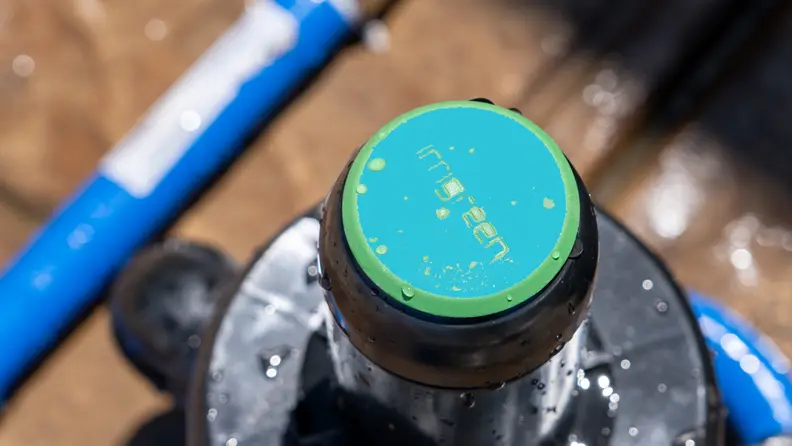 Bright green Irrigreen sprinkler cap shown next to blue piping over a tan patio.