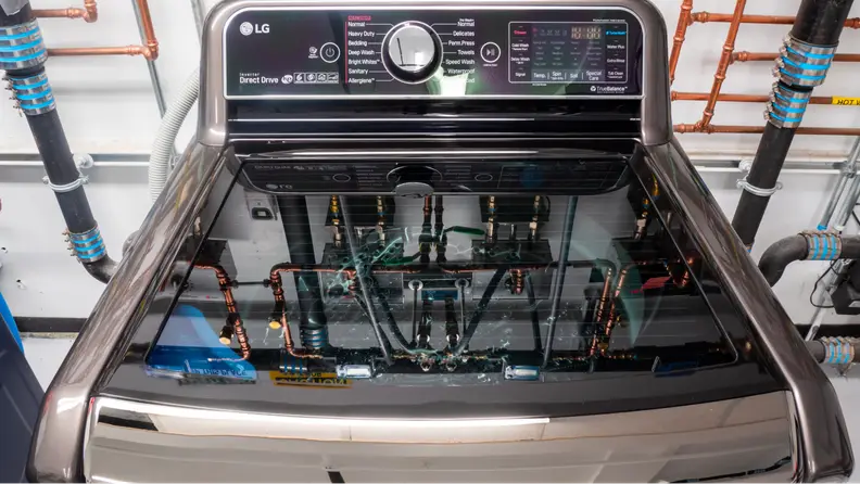 A close-up of the lid and control panel of the LG WT7900HBA top-load washing machine against a pipe-lined wall of our laundry testing lab.