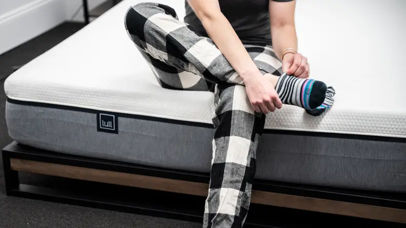 a person sits on the edge of the lull original putting on socks