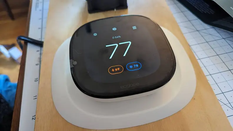 The Ecobee Smart Thermostat enhanced is shown mounted on a wood plank for testing.
